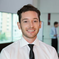Man in a white shirt and tie smiling in an office setting with blurred background
