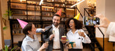 Group of people celebrating a birthday in an office setting with books and plants.