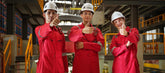 Three workers in red uniforms and white hard hats giving thumbs up in an industrial setting.