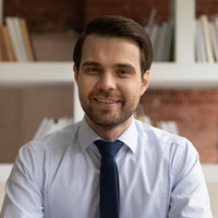 Man wearing a white shirt and blue tie in front of a bookshelf