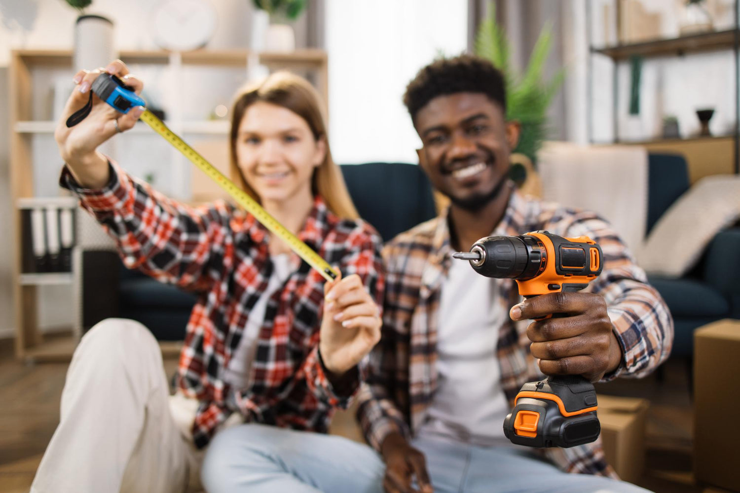Two people in a living room with a woman holding a tape measure and a man holding an electric drill.