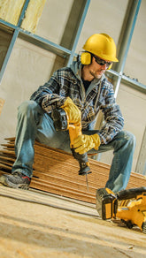 Worker in a construction site wearing safety gear and sitting on wooden planks.