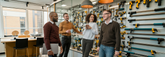 Group of people in a workshop or tool store with tools displayed on the wall.