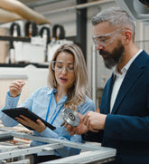 Two professionals, a man and a woman, working together in an industrial setting with machinery and tools.